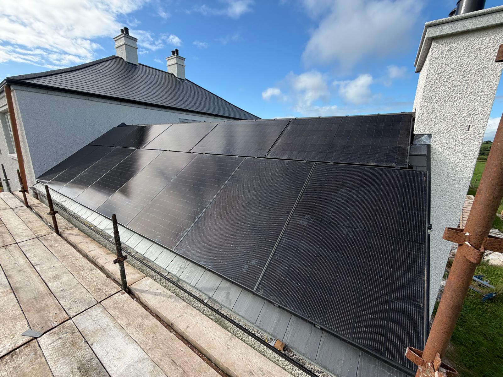 Black solar panels fitted to a slate roof beside a white rendered house